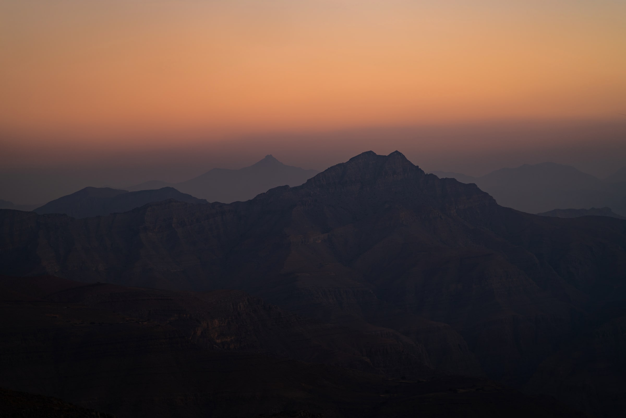 Layered mountain silhouettes beneath an orange dawn sky
