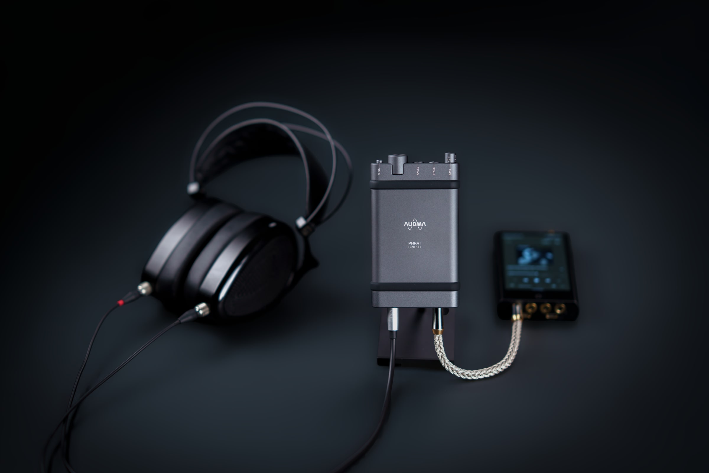 AUDMA Brioso portable headphone amplifier photographed with headphones and an audio player