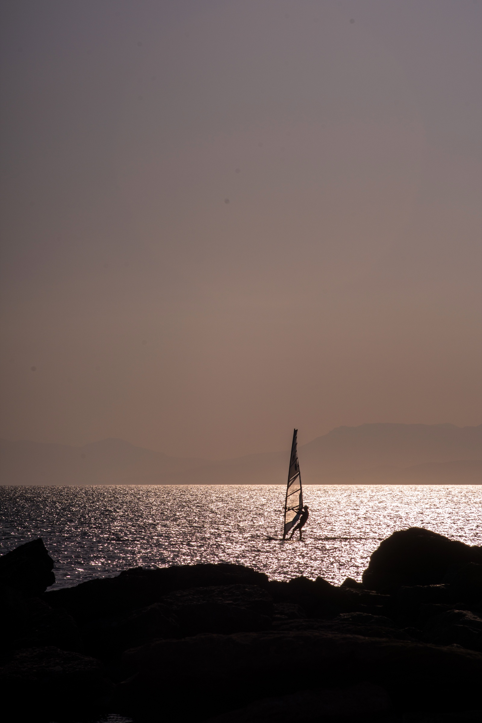 Windsurfer silhouetted on bright water at sunset