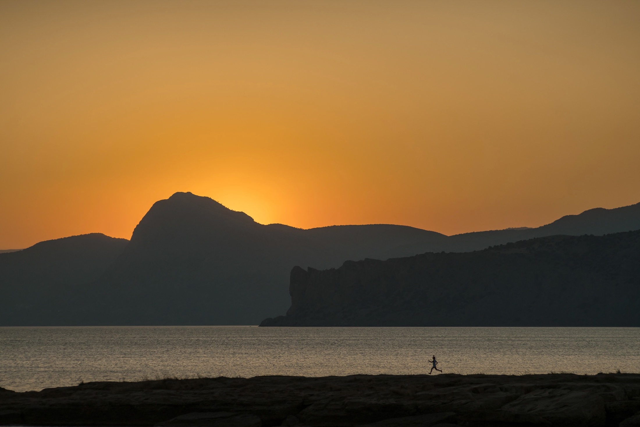 Runner passing a calm sea at sunset